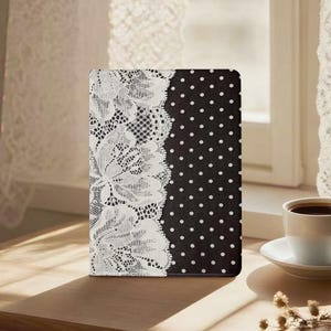 May include: A rectangular tablet case featuring a black background with a white polka dot pattern on the right side and a vertical panel of intricate white floral lace detailing along the left edge, creating a high-contrast visual design.