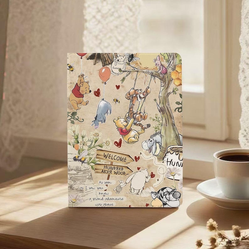 May include: A beige tablet case featuring a whimsical illustration of Winnie the Pooh and friends. The design includes characters like Pooh, Tigger, Eeyore, and Piglet, with a sign reading "Welcome Hundred Acre Wood". The case has a vintage, storybook aesthetic.