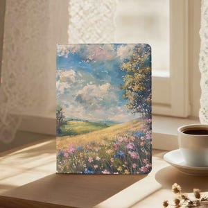 Puede incluir: Una funda rectangular para tableta con una pintura al óleo impresionista de un paisaje ondulado. La escena muestra un campo de trigo dorado lleno de flores silvestres rosas y azules bajo un cielo azul con nubes blancas y un gran árbol.