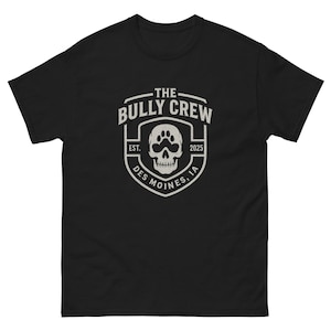 May include: Black t-shirt featuring a white graphic. The graphic includes the text "THE BULLY CREW" above a shield design with a skull and paw print. The text "EST. 2025 DES MOINES, IA" is also included.