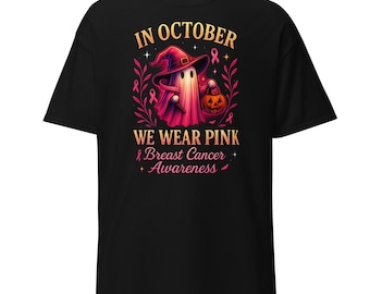 May include: Black t-shirt with a graphic of a ghost in a witch's hat holding a pumpkin. Text reads "IN OCTOBER WE WEAR PINK Breast Cancer Awareness".