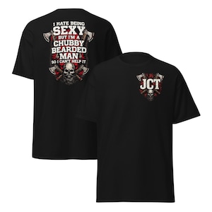 Puede incluir: Dos camisetas negras. Una presenta el texto "I HATE BEING SEXY BUT I'M A CHUBBY BEARDED MAN SO I CAN'T HELP IT" con hachas y una calavera. La otra camiseta tiene "JCT" con hachas y una calavera.