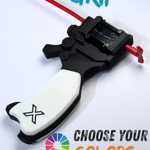 Puede incluir: Un agarre de lanzador Proto negro y blanco con un cordón rojo. El agarre tiene un mango blanco con un símbolo X negro y el texto "PROTO LAUNCHER GRIP" y "CHOOSE YOUR COLORS". También se muestra una rueda de colores colorida.