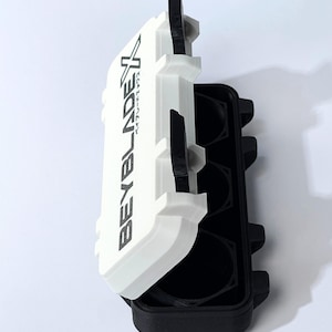 May include: A white and black plastic case with the text "BEYBLADEX" printed on the lid. The case is open, revealing black circular compartments. The case is designed to hold small items.