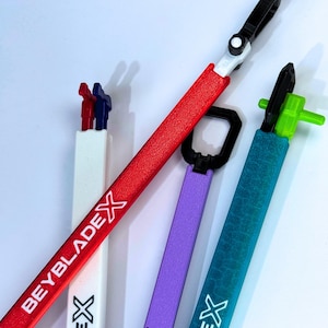 May include: Four Beyblade X launchers are displayed, in red, white, purple, and teal. Each launcher has a different coloured handle. The text "BEYBLADE X" and "X" are printed on the launcher's shaft. The launchers are set against a white background.