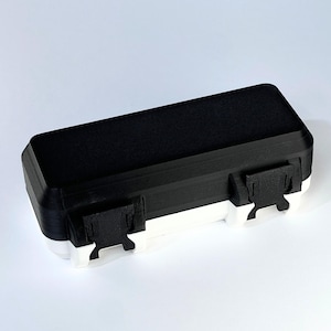 May include: A rectangular black and white storage box with two white clasps. The top of the box is black, and the bottom is white. The box is designed with a simple, modern aesthetic.