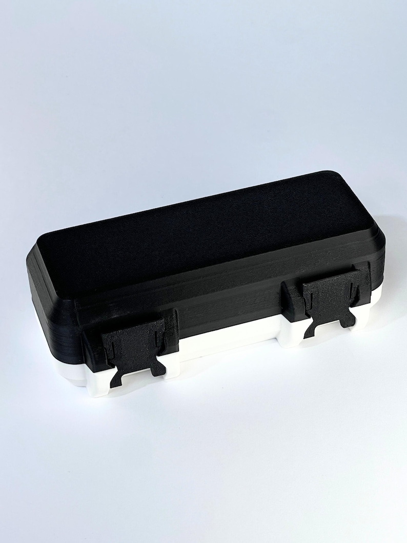 May include: A rectangular black and white storage box with two white clasps. The top of the box is black, and the bottom is white. The box is designed with a simple, modern aesthetic.