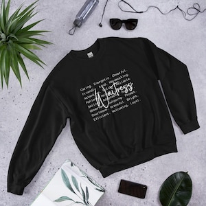 Könnte beinhalten: Schwarzes Sweatshirt mit dem Wort "Waitress" in Schreibschrift, umgeben von beschreibenden Wörtern wie "Caring", "Friendly" und "Cheerful". Das Sweatshirt hat einen Rundhalsausschnitt.