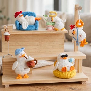 May include: A wooden tiered display stand holding six small crocheted white duck figures. The ducks are depicted in various activities, including lounging on a blue sofa, reading books, wearing sunglasses, and holding coffee mugs with the text COFFEE.