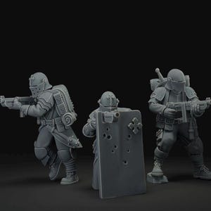 May include: Three gray miniature figurines of soldiers in armor, each holding a weapon. One figure holds a shield with bullet holes. The soldiers wear helmets and are posed as if in combat. The background is a solid black.