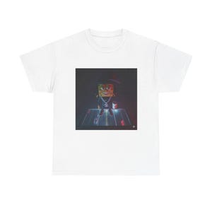 May include: White t-shirt with a graphic of a cartoon character wearing a hat and a chain. The character is standing on a platform with neon lights. The graphic has a dark, stylized aesthetic.