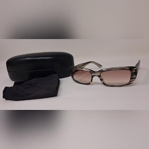 May include: Gray and brown gradient sunglasses with a black case and cleaning cloth. The sunglasses have a rectangular frame and gradient lenses. The case is oval-shaped and the cloth is folded.