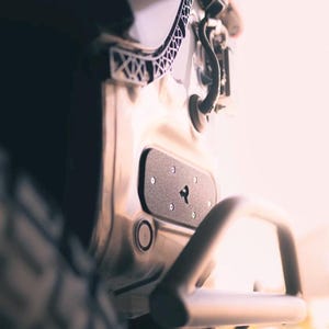 May include: Close-up of a vehicle's rear bumper and associated components. The bumper is silver with a black panel featuring a logo. A silver handle is attached. The image is well-lit, highlighting the details of the metal and design.