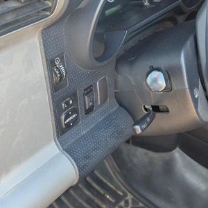 Könnte beinhalten: Innenansicht des Armaturenbretts eines Fahrzeugs mit Lenkrad, Instrumententafel und Bedienschaltern. Das Armaturenbrett ist hauptsächlich schwarz und grau, mit Spiegelbedienelementen und einem Kipphebel.