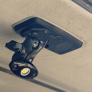 May include: Black LED light fixture with a rectangular base, mounted on a light-coloured surface. The light has a rounded, oval shape with a bright, white LED bulb. The fixture is attached with screws.