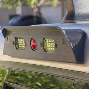 May include: A silver vehicle with a black spoiler featuring three lights: two square green lights and a central red light. The lights are embedded in a textured, dark gray panel.