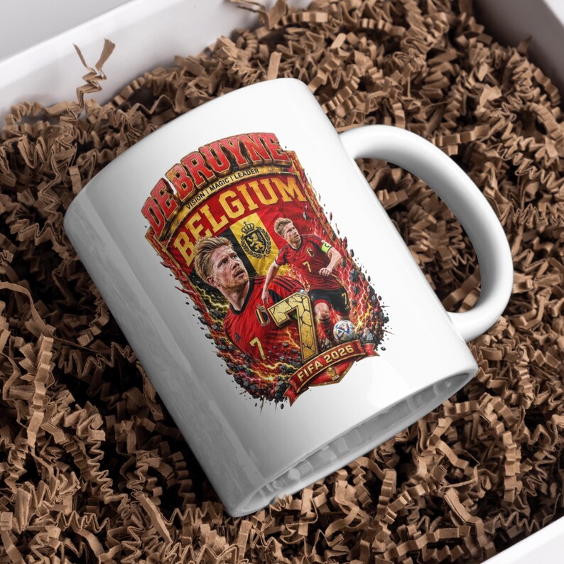 May include: A white ceramic mug featuring a graphic print of Kevin De Bruyne in a red Belgium soccer jersey. The design includes the text DE BRUYNE, BELGIUM, and FIFA 2026, along with a large number 7, fiery orange and red accents, and a soccer ball.