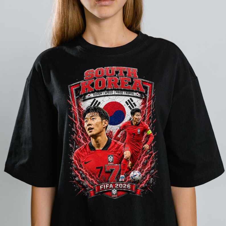 May include: A black t-shirt featuring a graphic print of a soccer player in a red jersey. The design includes the text SOUTH KOREA, FIFA 2026, and VISION | SPEED | PRIDE | KOREA, along with a red and blue circular emblem and red lightning effects.