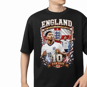 May include: A black t-shirt featuring a graphic print of a soccer player in a white England jersey with the number 10. The design includes the text ENGLAND, VISION MAGIC CAPTAIN, and FIFA 2026, along with a background of the England flag and lightning.