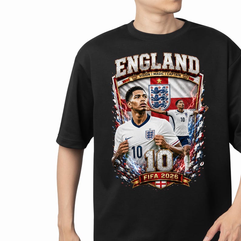 May include: A black t-shirt featuring a graphic print of a soccer player in a white England jersey with the number 10. The design includes the text ENGLAND, VISION MAGIC CAPTAIN, and FIFA 2026, along with a background of the England flag and lightning.