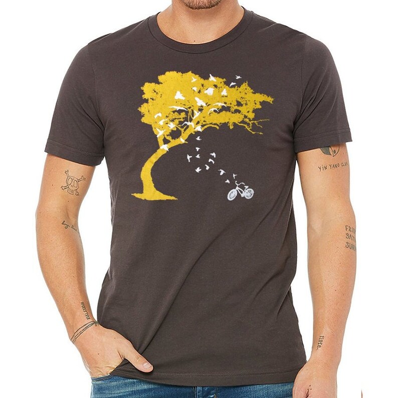 May include: A dark gray t-shirt with a yellow tree and white birds flying away from it. A white bicycle is under the tree. The text "Yin Yang Clan" is on the right sleeve.