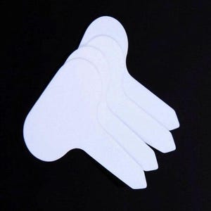 May include: A stack of white, T-shaped plant labels against a black background. The labels are made of a smooth, matte material and are designed for easy insertion into soil. The labels are used for gardening.