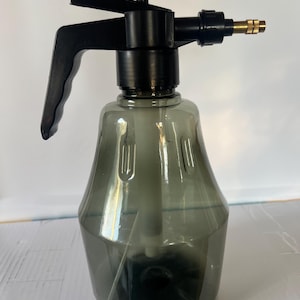 May include: A black and gray plastic spray bottle with a pump handle and adjustable nozzle. The bottle is transparent, allowing the liquid level to be seen. The nozzle has a brass tip. Ideal for gardening and cleaning.