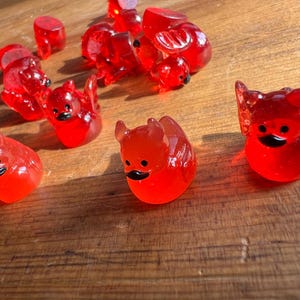 May include: A collection of translucent red bird-shaped figurines with black beaks and eyes. The figurines are scattered on a wooden surface, catching the light. Some have wing details.