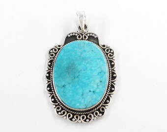 Puede incluir: Colgante ovalado de turquesa con marco de filigrana plateado. El colgante presenta una piedra azul brillante con vetas naturales. El marco tiene un diseño decorativo y un lazo para una cadena.