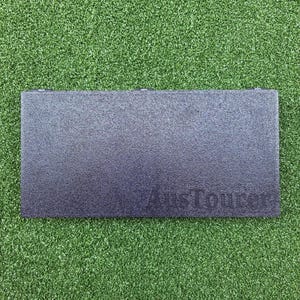 May include: A dark grey rectangular object with a textured surface. The text "AusTourer" is imprinted on the lower right corner. The object is set against a green, grassy background.