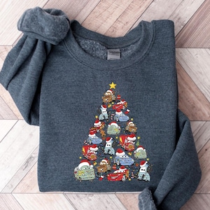 May include: A dark gray sweatshirt featuring a Christmas tree design made of cartoon cars. The cars are decorated with Santa hats and a gold star at the top. The sweatshirt is made of a soft material.