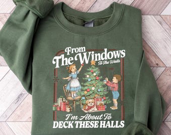 May include: Green sweatshirt with a festive graphic. The graphic features a vintage illustration of a Christmas tree being decorated by two children, with the text "From The Windows To The Walls" and "I'm About To Deck These Halls".