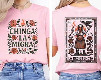 May include: Pink t-shirt with the text "CHINGA LA MIGRA" surrounded by floral elements on the front. The back features a graphic of a person holding a torch, with the text "LA RESISTENCIA" below.