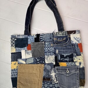May include: A patchwork denim tote bag with a variety of blue denim patches, corduroy, and other fabrics. The bag features a denim handle and a pocket on the front. The bag is a unique, handmade item.