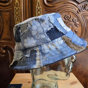 May include: A bucket hat constructed from various patches of blue denim fabric, featuring a mix of light and dark washes, floral patterns, and corduroy textures. The hat has visible stitching throughout the patchwork design and a wide brim.