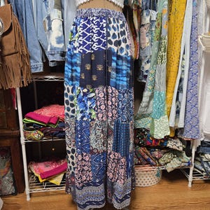 May include: A floor-length skirt featuring a patchwork design with various blue, white, and pink floral and geometric patterns. The skirt has an elasticized waistband with a drawstring and a loose, flowing silhouette made of multiple fabric panels.