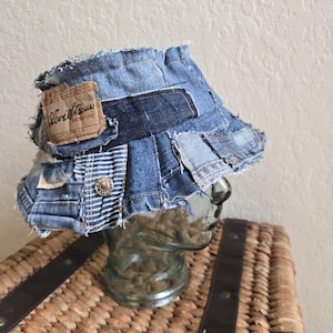 May include: A patchwork denim bucket hat with a distressed, vintage aesthetic. The hat features various shades of blue denim, with visible stitching and frayed edges. A Levi Strauss label is sewn on the side. The hat is displayed on a glass head.