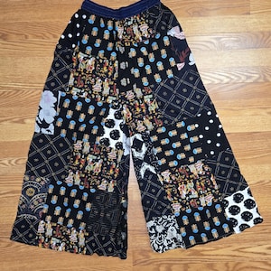 May include: Black patchwork pants with a wide leg design. The pants feature a variety of patterns, including floral, polka dots, and geometric shapes. The fabric appears to be lightweight, with a dark blue waistband.