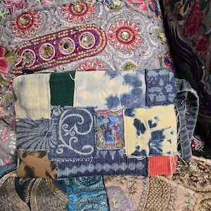 Könnte beinhalten: Eine Patchwork-Denim-Clutch mit einer Vielzahl von Stoffflicken, darunter Batik, Cord und gemusterter Denim. Die Clutch hat ein kleines, farbenfrohes Bild und einen Griff. Der Hintergrund ist ein dekoratives Textil mit floralen Stickereien und Verzierungen.