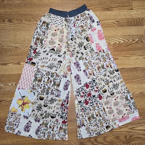 Może przedstawiać: Szerokie spodnie z patchworkowym wzorem z różnymi wzorami i kolorami. Spodnie mają talię ze sznurkiem i mieszankę motywów kwiatowych, geometrycznych i figuratywnych w odcieniach bieli, różu, czerwieni i zieleni.