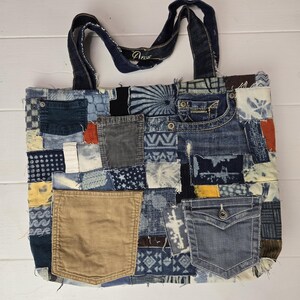 May include: A patchwork tote bag made from various denim pieces, featuring different shades of blue, brown, and tan. The bag includes pockets and a corduroy pocket. The handles are made of denim. The bag is on a white wooden surface.