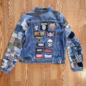 May include: A light blue denim jacket with patchwork sleeves and various band patches on the back, including "Misfits," "Guns N' Roses," and a skull. The jacket has a classic collar and button closures.