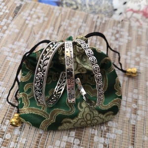 May include: Three silver-toned metal bangles featuring distinct embossed designs. One bangle displays a floral vine pattern, another features a repeating butterfly motif, and the third is decorated with a continuous row of small rose blossoms.