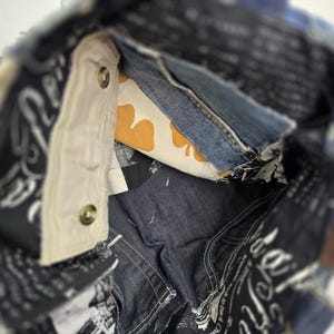 May include: A patchwork denim tote bag with a navy blue handle. The interior features a light-colored pocket with two buttons, a denim pocket, and a yellow and white patterned fabric. The bag is made from various denim pieces.