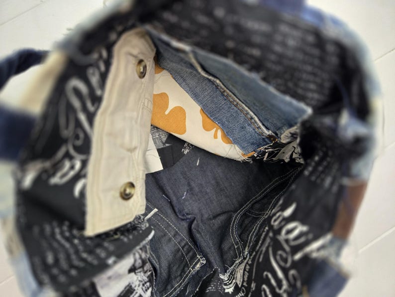 May include: A patchwork denim tote bag with a navy blue handle. The interior features a light-colored pocket with two buttons, a denim pocket, and a yellow and white patterned fabric. The bag is made from various denim pieces.