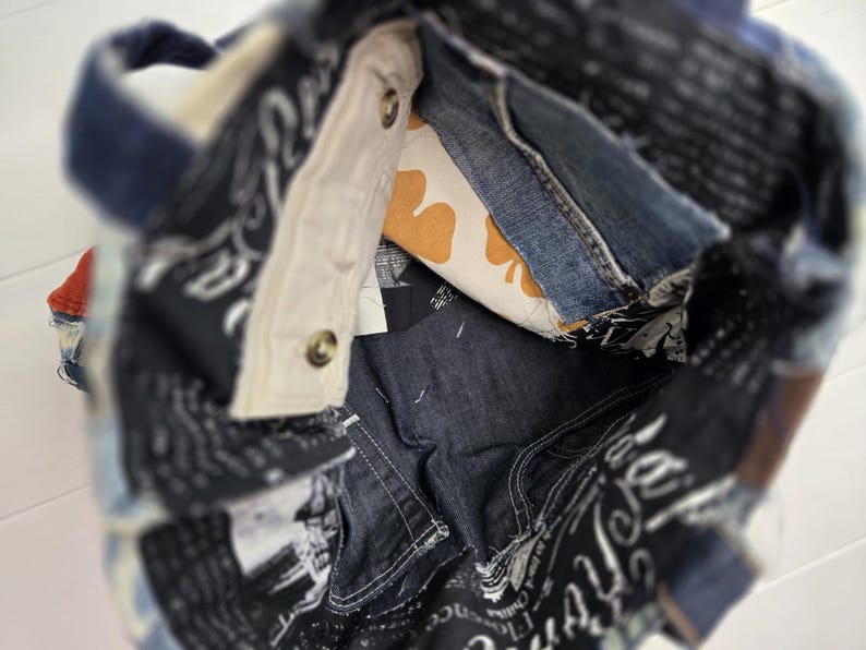 May include: A denim tote bag with a patchwork design. The bag features a mix of blue denim, patterned fabric, and a cream-colored interior with a yellow clover pattern. The bag has a handle and is constructed with visible stitching and metal button closures.