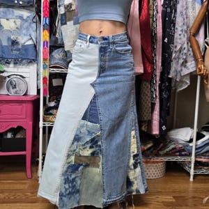 May include: A light blue crop top and a long denim skirt. The skirt is a patchwork design, combining light and medium blue denim with various patches. The skirt has a high waist and a long, flowing silhouette.