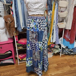 May include: A white strapless tube top with a textured knit pattern paired with a long, flowing skirt featuring a patchwork design of blue, white, and navy patterns including polka dots, floral motifs, and geometric shapes with an elastic waistband.