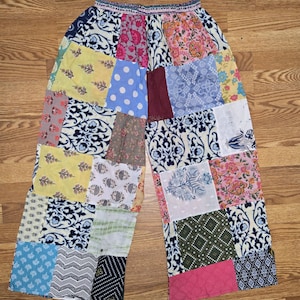 Może przedstawiać: Spodnie patchwork z szerokimi nogawkami. Spodnie posiadają różnorodne kolorowe łaty materiału z kwiatowymi, groszkowymi i geometrycznymi wzorami. Pas jest w jednolitym kolorze z ozdobnym wykończeniem.