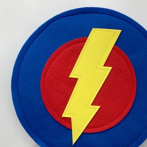 May include: A blue felt circle with a red felt circle in the center. A yellow felt lightning bolt is centered on the red circle.